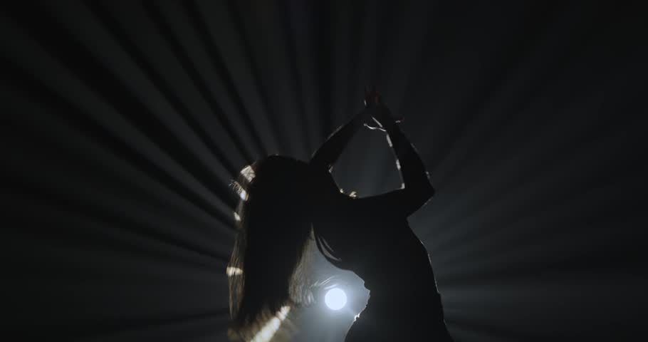 Silhouette of a female dancer performing on a dark stage, back lit by dramatic volumetric light rays with copy space. Concepts related to dance, self discovery, album covers, singles, or podcasts