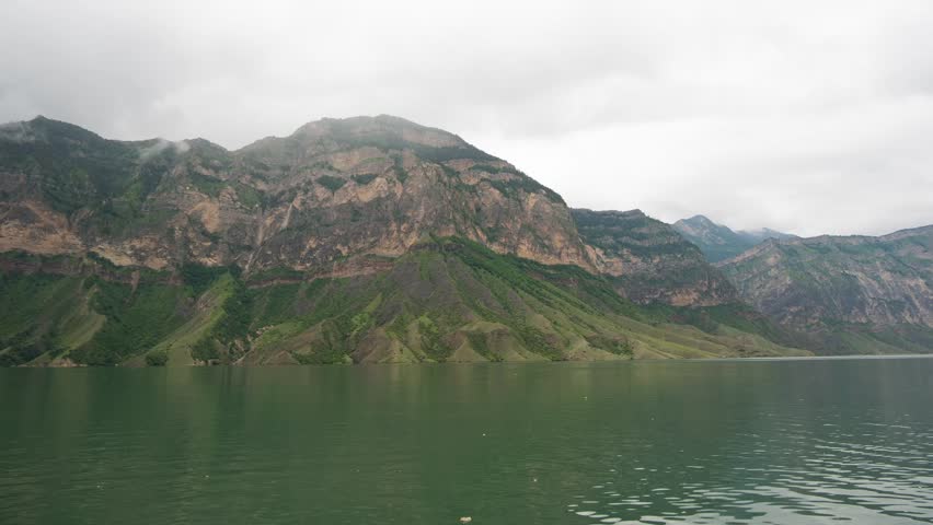 Rain clouds fill the sky over a large mountain lake that is bordered by tall mountains. 