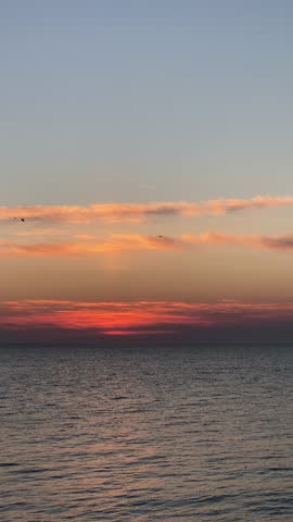 Vibrant orange and pink clouds above dark ocean water at dawn before sunrise
