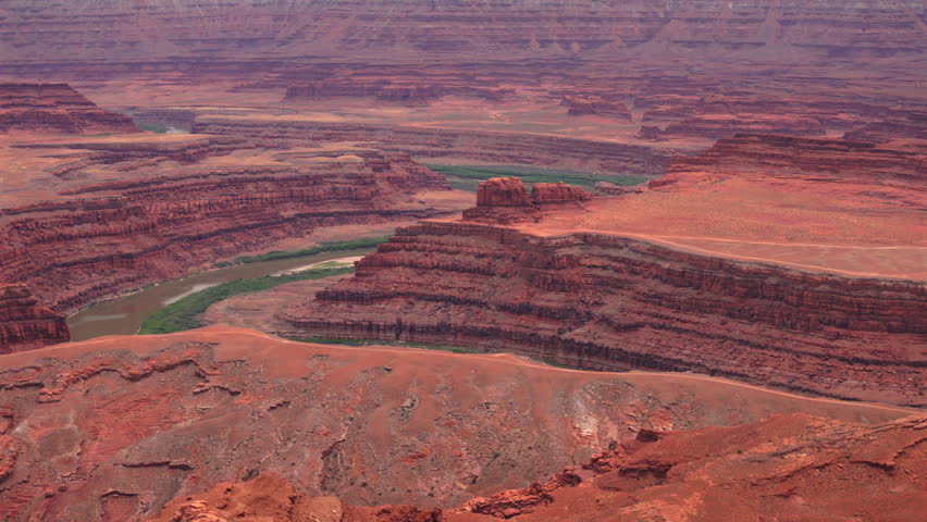 Dead Horse Point State Park in Utah reveals stunning red rock canyon formations with the Colorado River winding through layered sandstone cliffs and mesas under hazy skies.