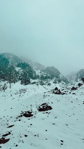 4K vertical view of snowfall in mountains during winter season at Chandanwari, Jammu and Kashmir, India. Winter background. Snow covered Himalayas and stormy clouds in sky. Nature landscape.