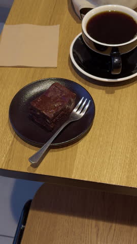 Cup of black coffee with chocolate brownie on plate, fork and napkin on wooden cafe table