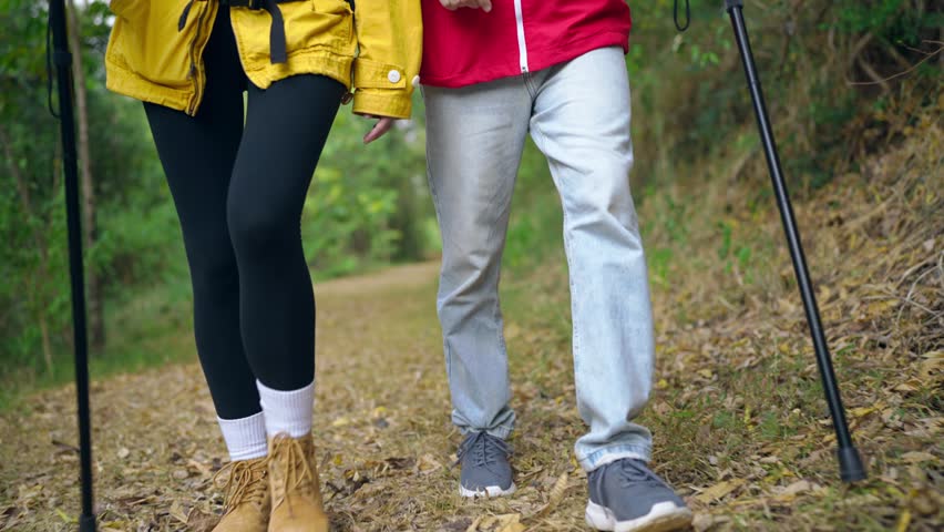 Close up of two hikers walking together on a trail in the mountains. Active young travelers exploring forest and nature in peaceful countryside landscape, enjoying outdoor adventure with happiness.