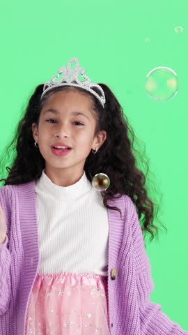 Face, bubbles and girl in costume in studio for pretend playing, princess and imagination. Childhood, fantasy and happy kid with wand, crown and toys for fun, dress up and magic on green background