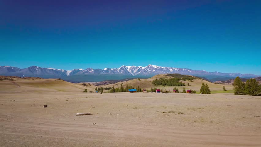 A beautiful landscape, the arid steppe of the Altai Mountains in Russia, with high mountains with snow-capped peaks in the distance
