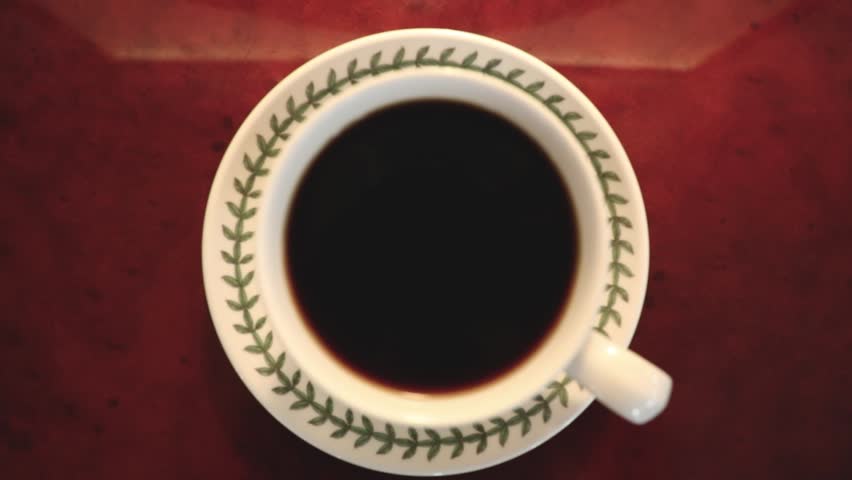 Top-down view of a cup of black coffee on a patterned saucer placed on a round wooden table