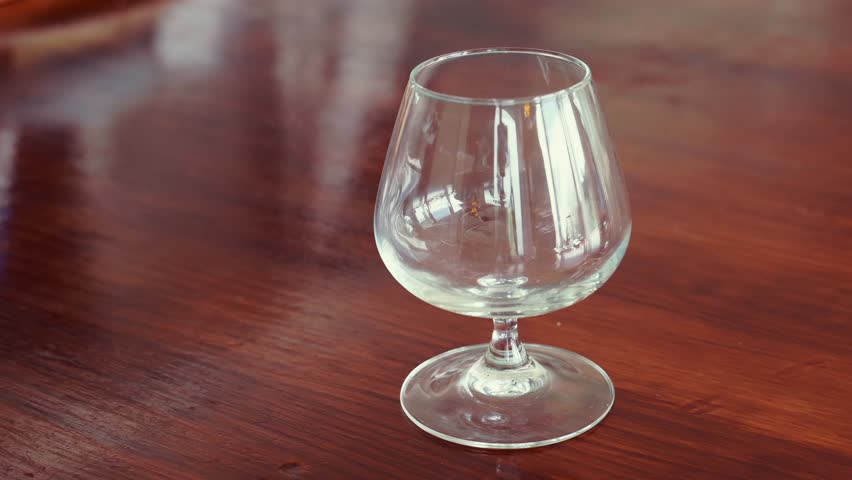 An amber beautiful rich whisky being poured into a crystal glass on a wooden table.