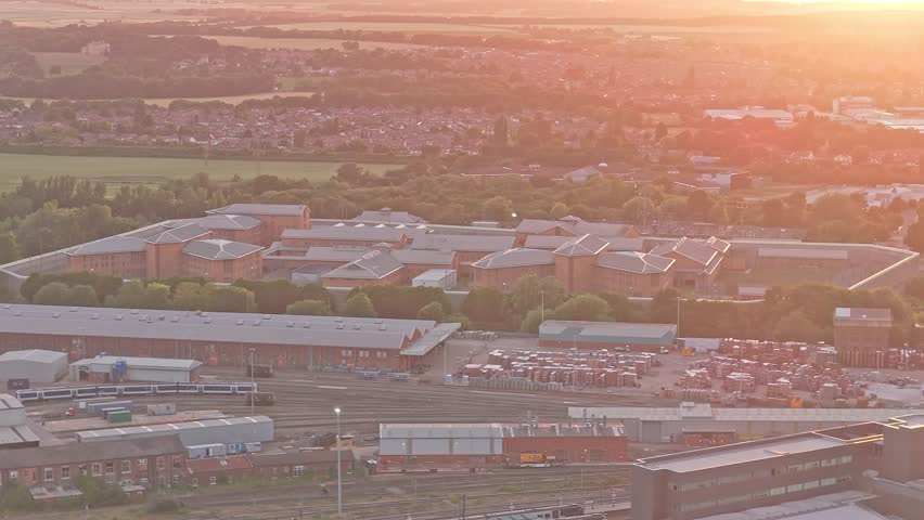 Large secure prison complex stands beyond an extensive railway depot with tracks, maintenance buildings and rolling stock, at Marshgate, Doncaster DN5 8UX, South Yorkshire, England, United Kingdom