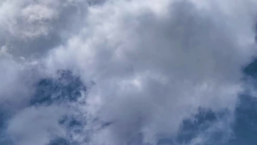 Dense white clouds covering a blue sky with varying shades and textures, suggesting a partly cloudy or overcast weather condition.