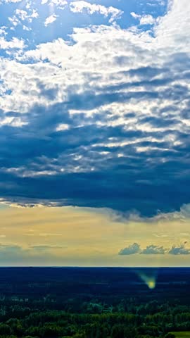 Dramatic clouds move over a forest landscape as sunlight breaks through at sunset