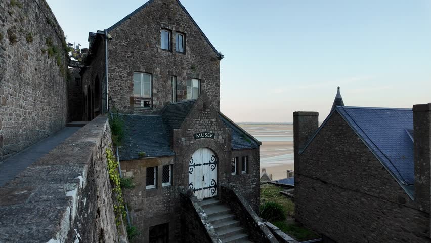 Front entrance of the museum at Mont Saint-Michel seen from an elevated viewpoint, highlighting authentic medieval stone architecture, steep stairways, and the timeless atmosphere .
