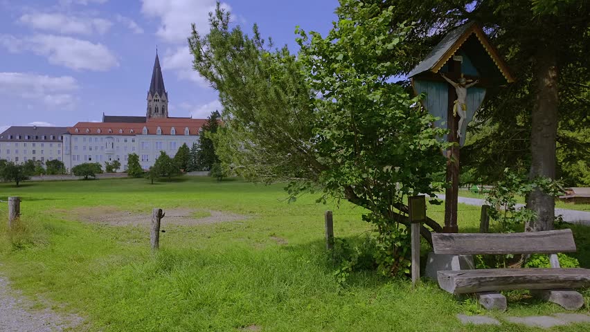 Wayside cross and bench, with Saint Ottilien Archabbey, monastery of the Missionary Benedictines in the background; Eresing, Bavaria, Germany
