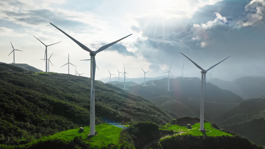 Wind turbines operating on green mountain ridges under a bright cloudy sky, generating clean renewable energy.