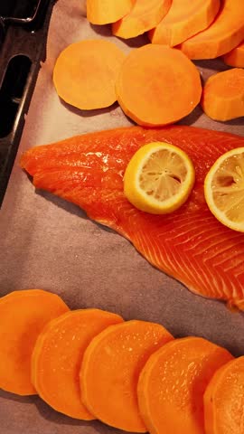 Delicious raw salmon fillet with fresh lemon slices and sweet potatoes on a baking sheet. Preparation of a healthy, homemade pescatarian meal