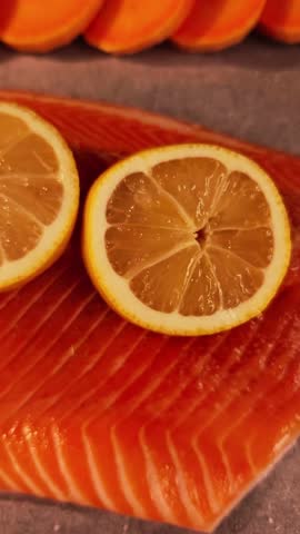 Close up of a delicious raw salmon fillet seasoned with fresh lemon slices and arranged with sweet potatoes on a baking sheet before cooking