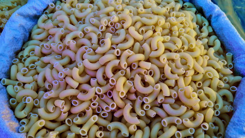 A sack of uncooked elbow macaroni pasta displays evenly shaped pieces with smooth surfaces and uniform colour. Neatly arranged pasta creates a tidy presentation within the sack.