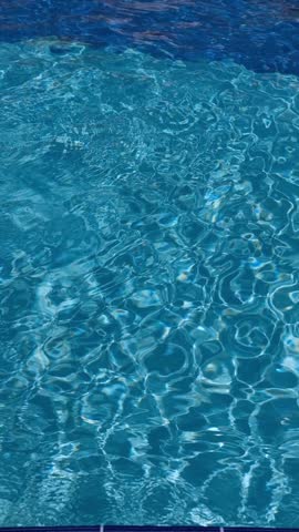 Pure blue water in the pool with light reflections. Slow motion. 4k vertical footage