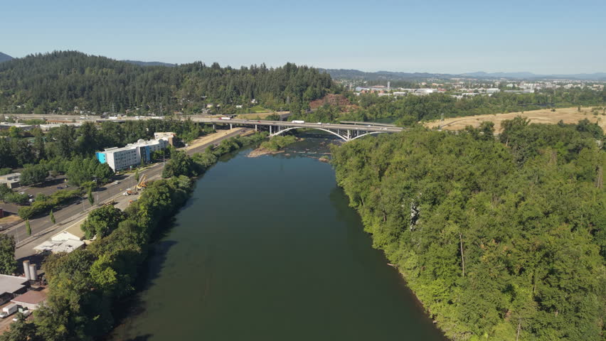 Willamette River drone footage in Eugene, Oregon, showing the water flowing beneath a roadway bridge on a clear summer day.