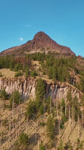 Nevado de Colima in Jalisco, Mexico, showcasing the rugged mountain peak, rocky cliffs and forested slopes beneath a clear blue sky. Vertical view