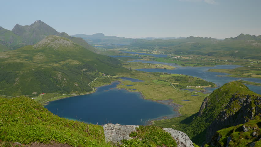 High viewpoint looks over a deep blue lake, winding valleys, farms, and distant hills under clear daylight skies.