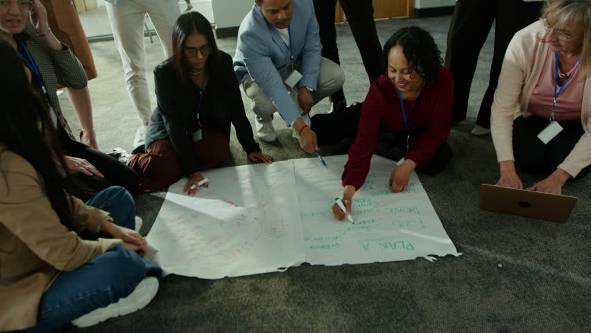 A group of colleagues actively collaborates on a large paper plan during a meeting. They are engaged in thoughtful discussion, sharing ideas and working together effectively on their project.