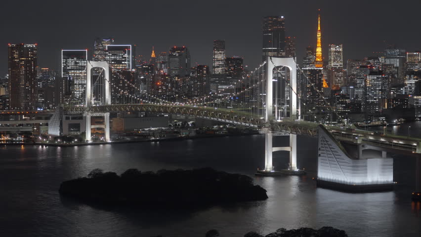 Locked-off shot showing the Rainbow Bridge and Tokyo skyline at night from Odaiba, Tokyo, Japan. 