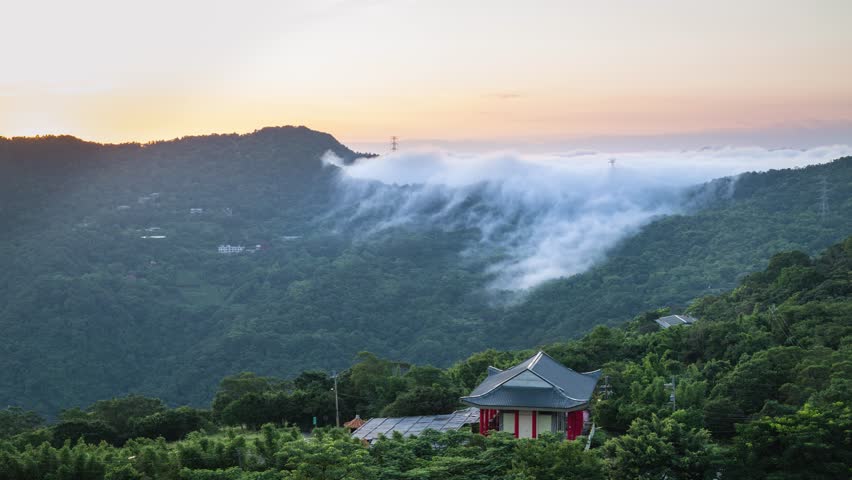 Breathtaking morning view of rolling clouds over green mountains at sunrise with a traditional Asian temple in the foreground in Xindian, Taiwan.
