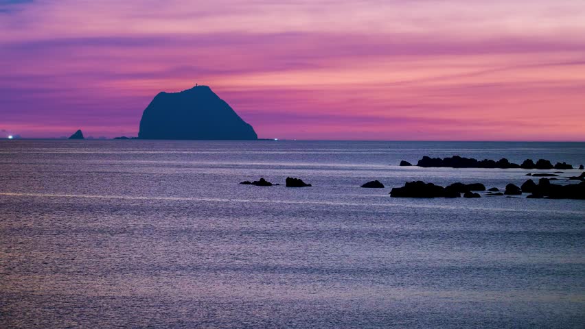 Scenic view of Keelung Islet during dawn with a vibrant pink and purple morning sky, calm ocean water, and coastal rocks in Keelung, Taiwan.