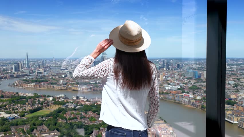 Rear view of a tourist woman looking at the panoramic view of the skyline of London, England, during a sunny summer day