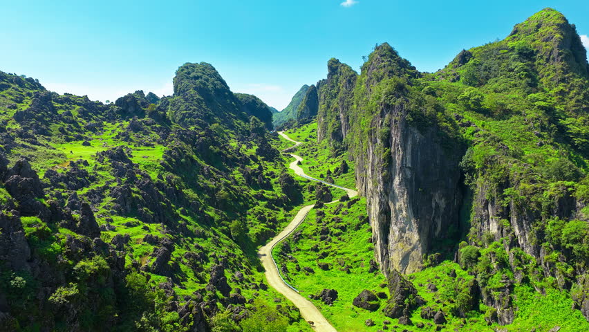 Winding road passing through green karst mountain valley under clear blue sky.