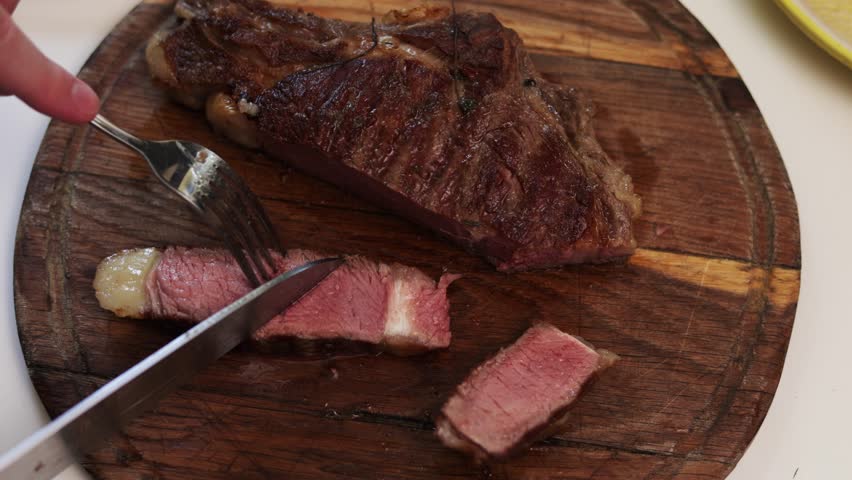 Close-up view of a perfectly cooked steak being sliced into tender pieces on a textured wooden cutting board