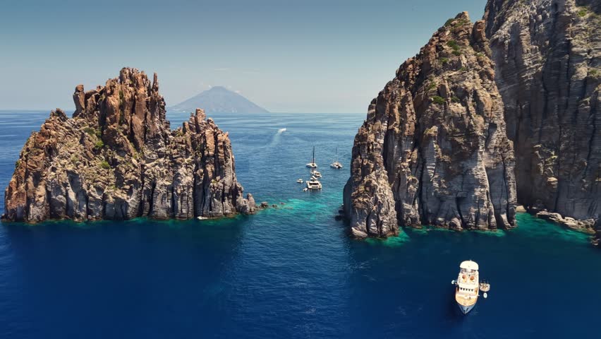 Flying over crystal clear turquoise sea water near Panarea and Basiluzzo rocks. cenic coastal landscape of Aeolian islands, Sicily, Italy. Catamarans anchored near cliffs of Basiluzzo