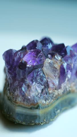 Sparkling macro shot, purple amethyst geode with its violet crystals layered agate base slowly rotating on white background, natural raw texture, facets. Purple amethyst gemstone crystal. Vertical