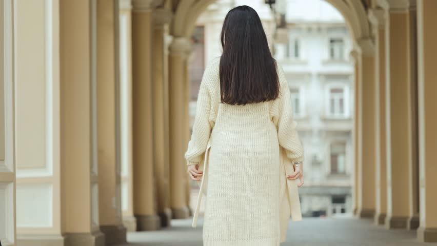 Young woman twirls gracefully with open arms beneath a sunlit city arcade in a carefree moment. Freedom, movement, fashion, confidence, happiness, lifestyle, femininity, positivity.