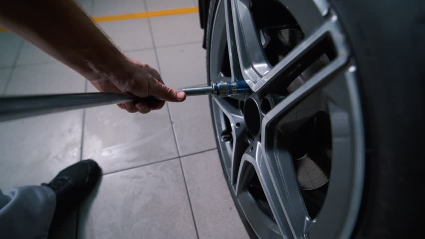 A mechanic at a tire shop loosens a car wheel using a large adjustable wrench.