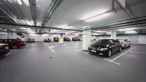 Many cars stand in underground parking with piping and illumination