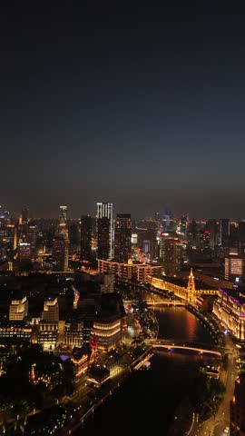 Magnificent aerial night scene of a vibrant modern city in Shanghai, China with skyscrapers and buildings brightly illuminated by golden lights, showcasing the urban landscape and a winding river with bridges.