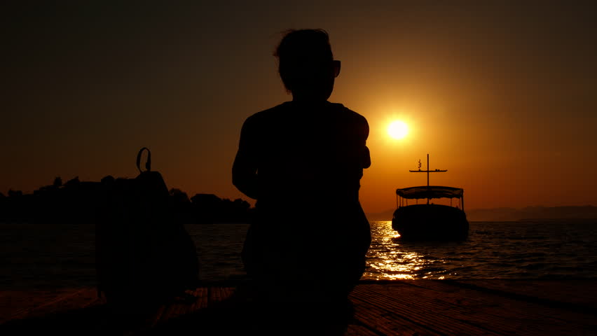 Female meets the sunset on pier. A female sitting on pier and meet the yacht in the dusk harbor