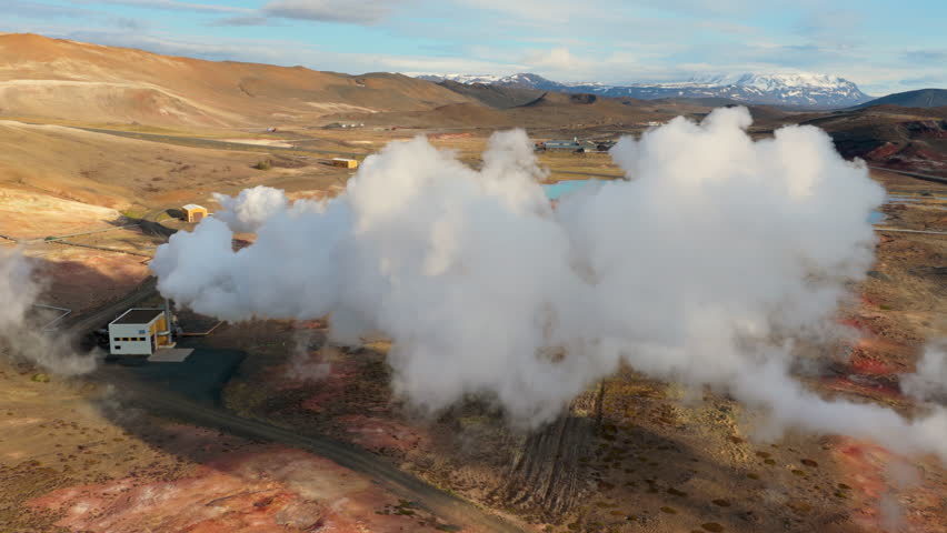 Steam emanates from volcanic site. Vast geothermal installation amid volcanic and mountain scenery