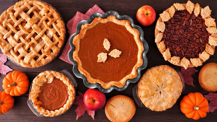 Assortment of homemade fall pies. Apple, pumpkin and pecan. Top down view table scene on a dark wood background. Slow rotating zoom motion.