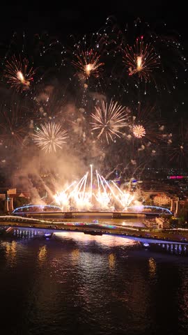 Colorful fireworks exploding in the dark sky over a river and illuminated bridge, creating a vibrant celebration and reflecting beautifully on the water during a grand festive event at night, Bangkok, Thailand.