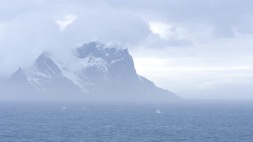 Antarctica Dramatic Mountain Covered in Mist and Clouds Close Up with Blow Hole Spray from Humpback Whales. Exciting Adventure Travel.