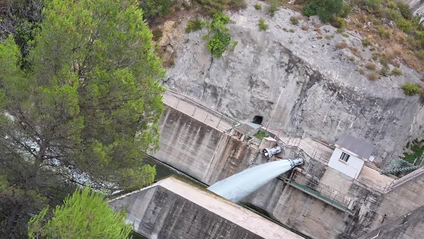 Slow motion shot of powerful water discharge from dam pipe into river channel. Water pressure release mechanism at hydroelectric reservoir station on sunny day.