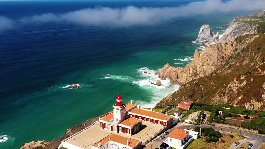Take a look at Cabo da Roca from the sky aerial view. Watch the waves crash on the rocks and enjoy the view of the lighthouse near the coastline during a sunny day.