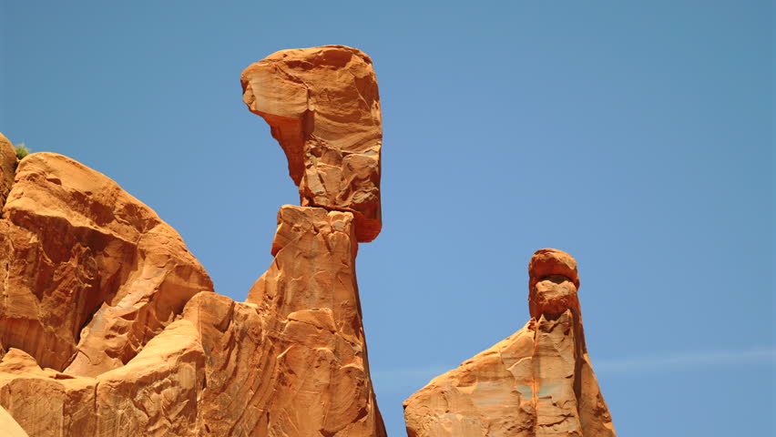 Dramatic red sandstone hoodoo rock formations with distinctive mushroom-shaped caps rise majestically against a vibrant clear blue sky in the American Southwest desert landscape on a sunny day.