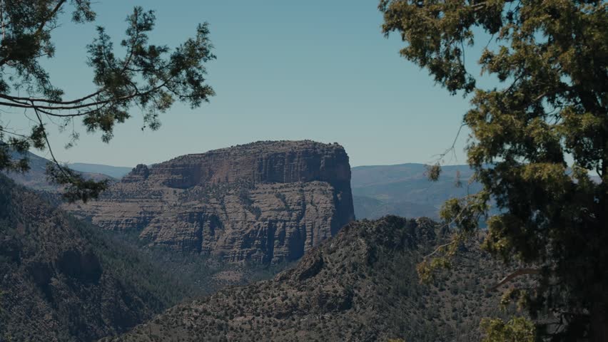 Layered rock butte in Morocco rising above wooded canyon slopes framed by juniper trees