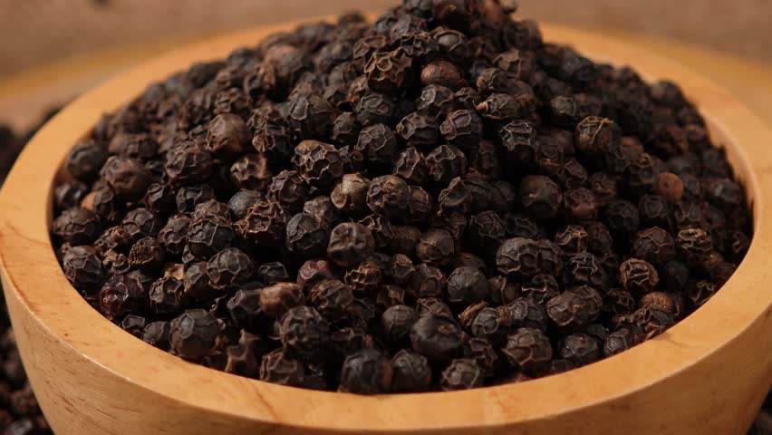 Dried black peppercorns in a wooden bowl.