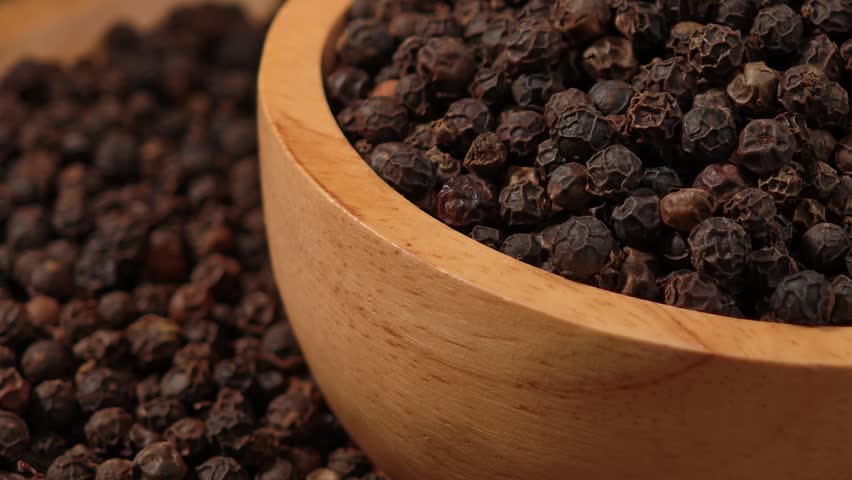 Dried black peppercorns in a wooden bowl.