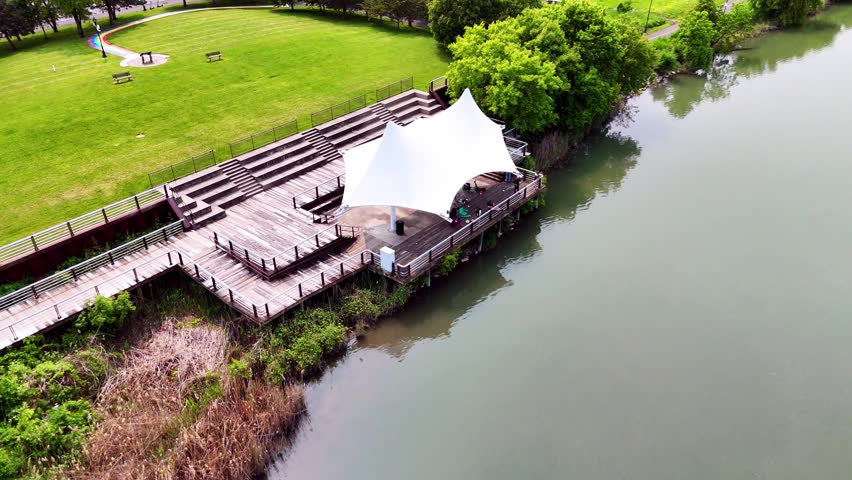 A public dock shaded by a fabric structure intended to be utilized as a pavilion as people swing their fishing rods and cast their lures into the surrounding water.