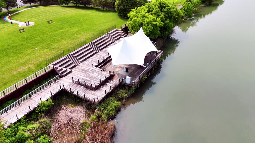 A public dock shaded by a fabric structure intended to be utilized as a pavilion as people swing their fishing rods and cast their lures into the surrounding water.